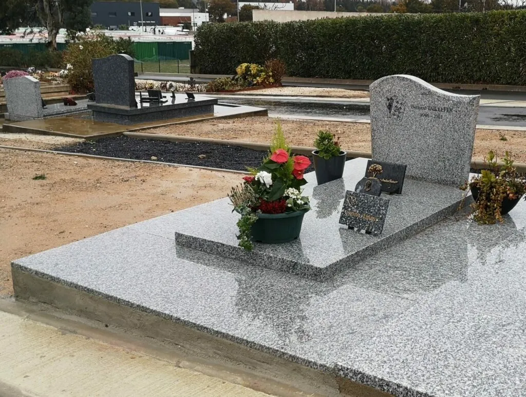 Monument funéraire en granit posé en cimetière et orné de potées de fleurs